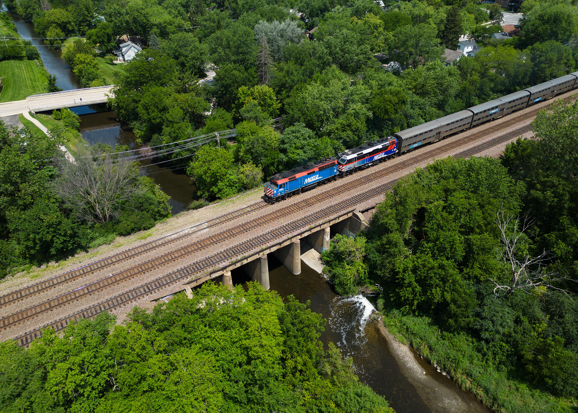 a outbound Metra train crosses over the Fox river in Geneva, IL. as captured from a drone.